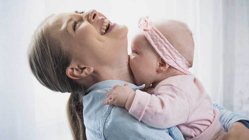 attachment - mom smiling and looking up while her baby kisses her neck