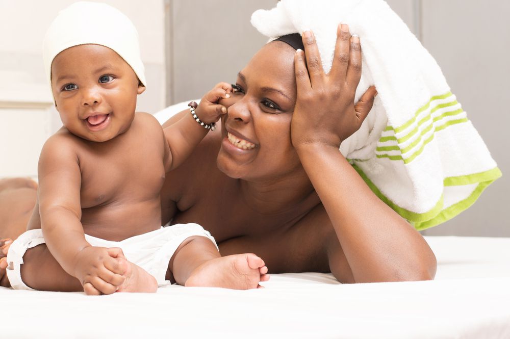 young mother in a towel is lying in bed, plays lovingly with baby after bath