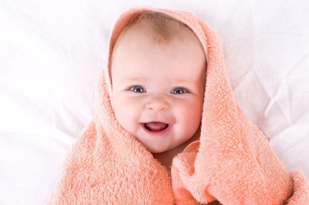 a cute baby smiling wrapped up in a towle and laying on a bed