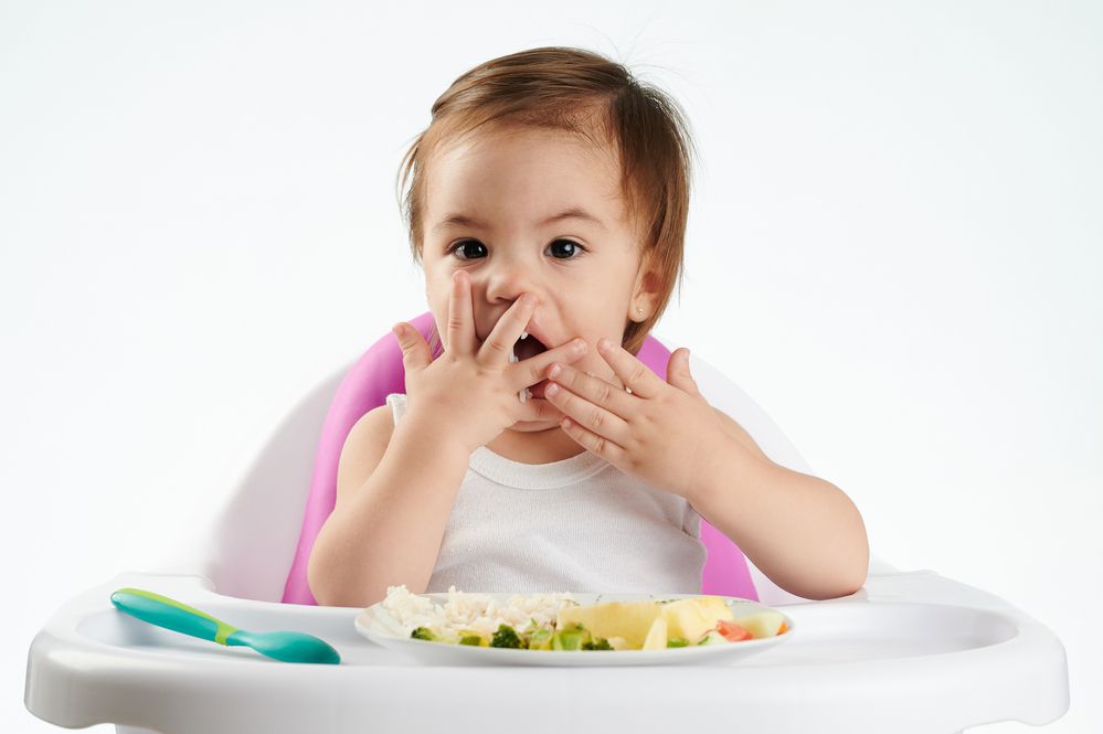 Baby eating with hands on high chair 