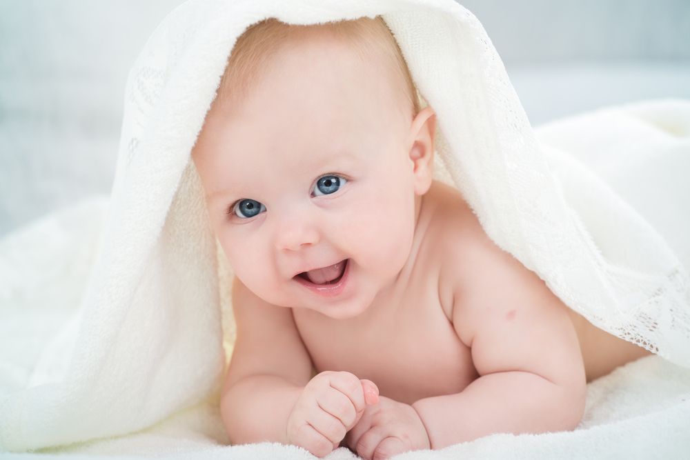 Curious baby laying on stomach staring at camera with blanket over his head
