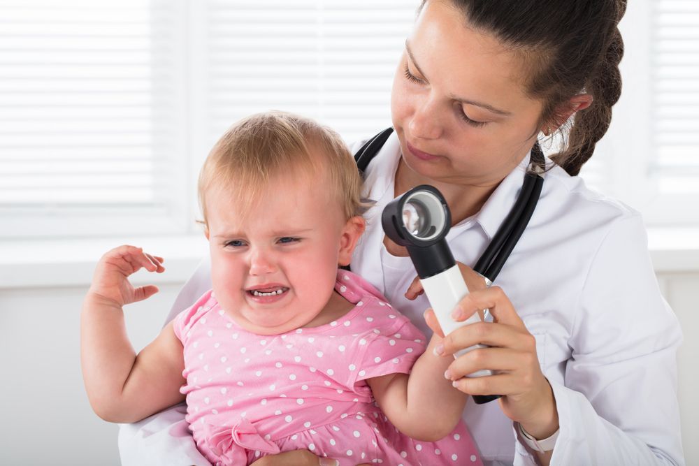 Baby with ear infection crying in doctors arm while doctor tries to sooth her and look in ear