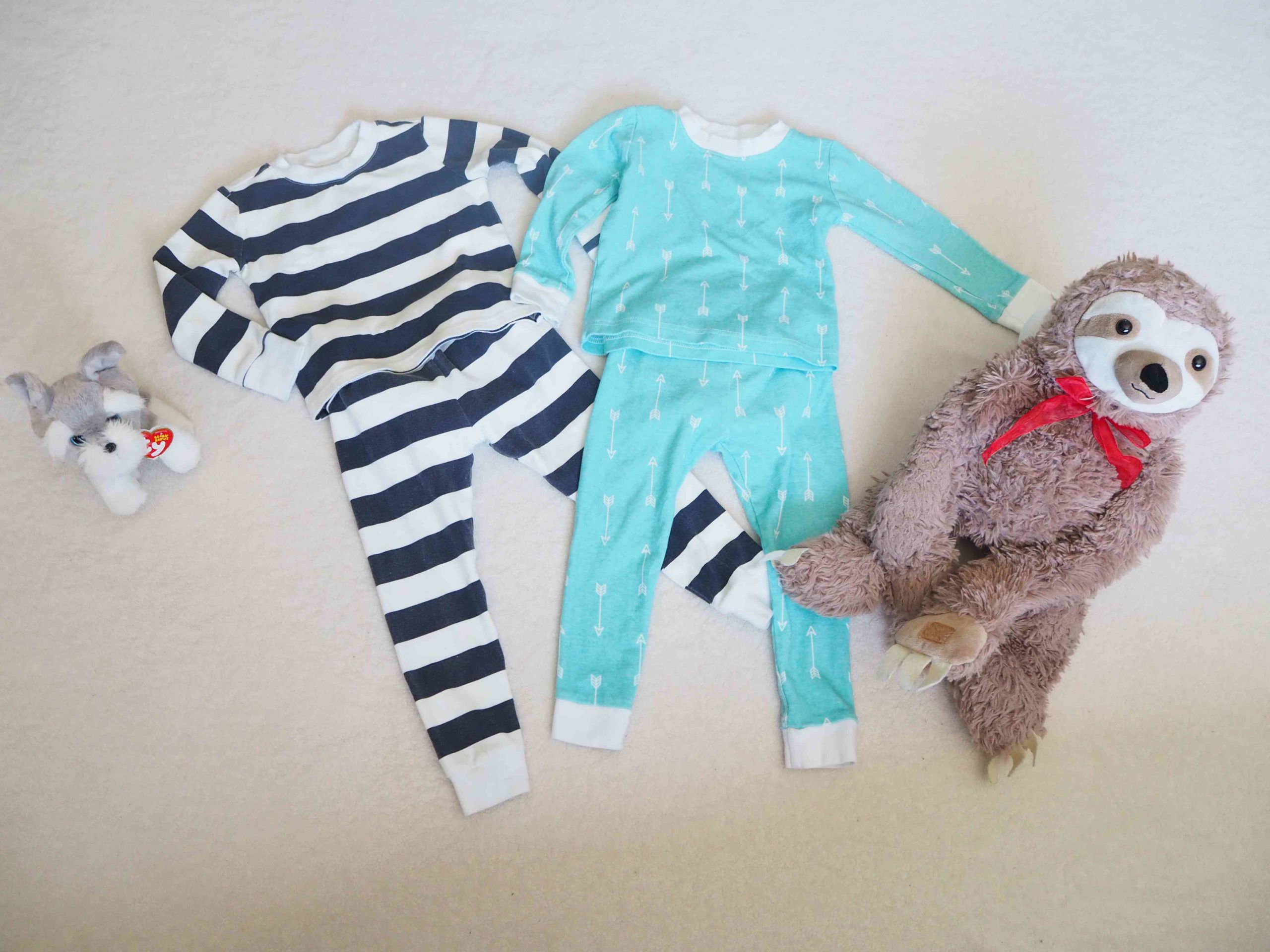 two pairs of peejamas laid out on the floor next to stuffed sloth toy