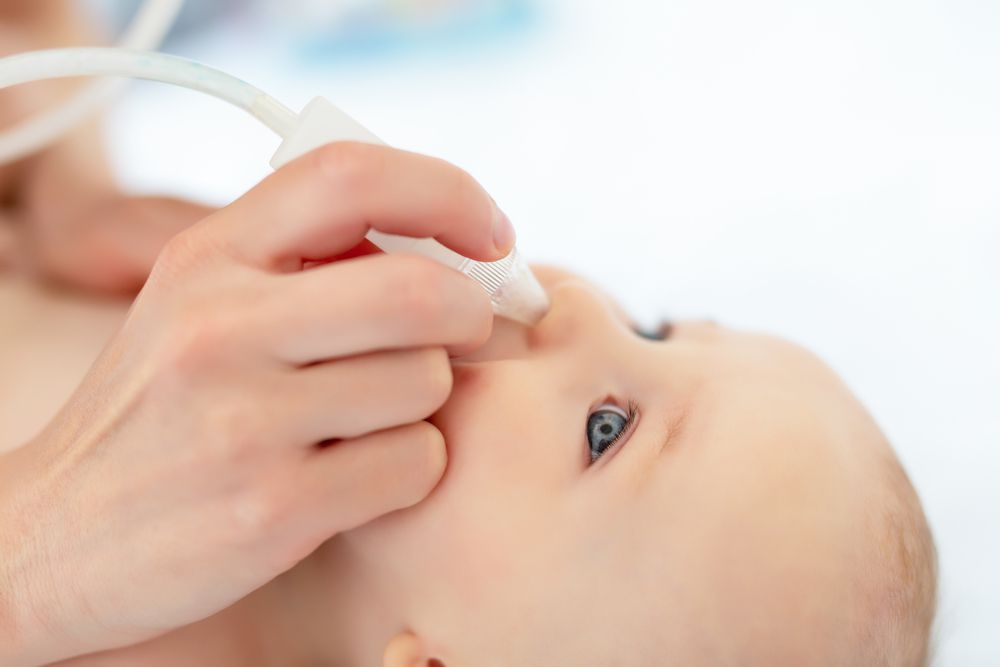 mom using nasal aspirator to suck mucus out of baby's nose