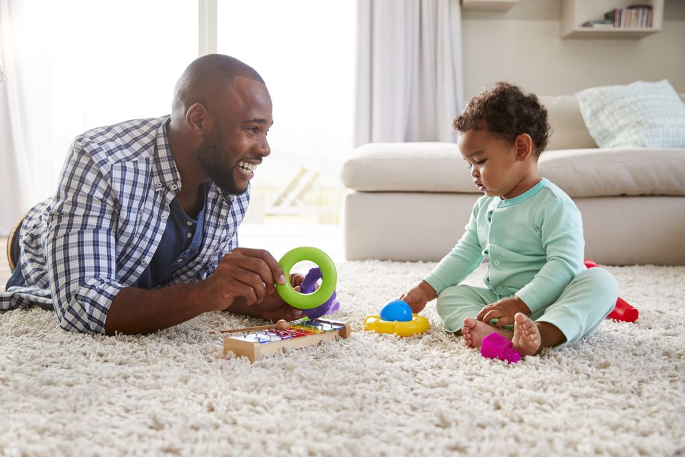 Black dad and toddler son playing on floor at home, close up
