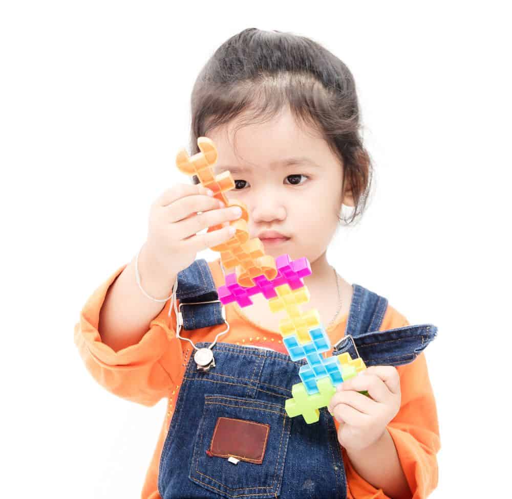 toddler in overalls focused on pulling apart an interlocking toy
