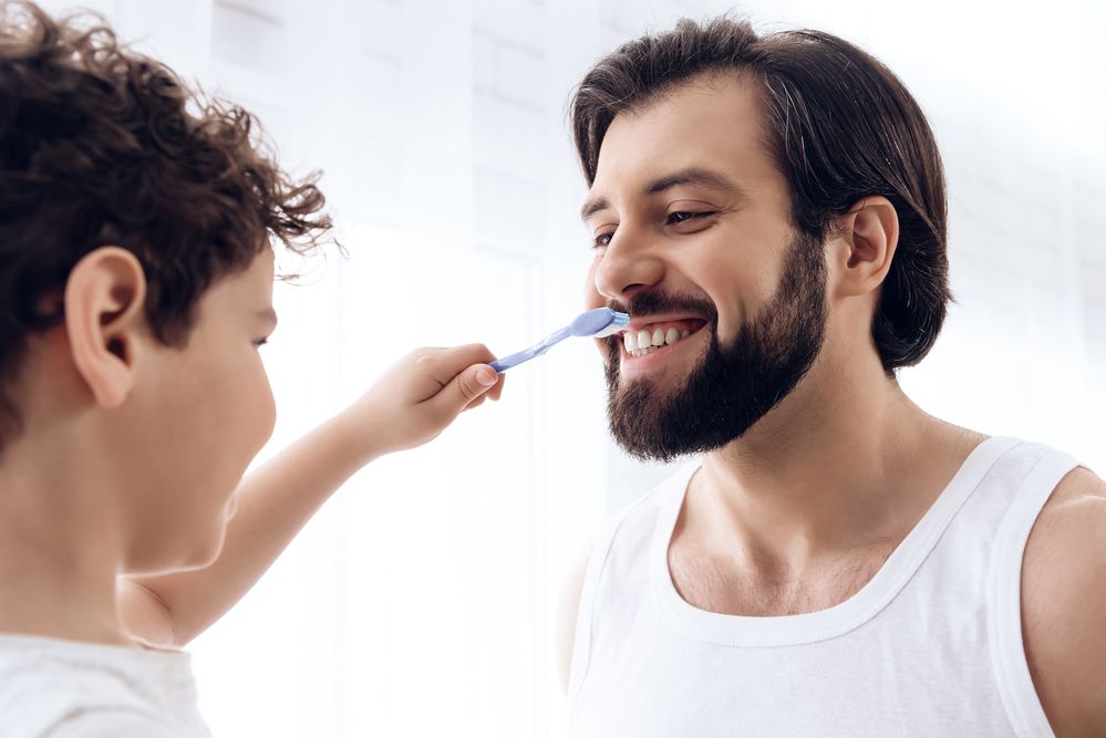 dad and toddler having fun brushing teeth together while the toddler brushes dads teeth