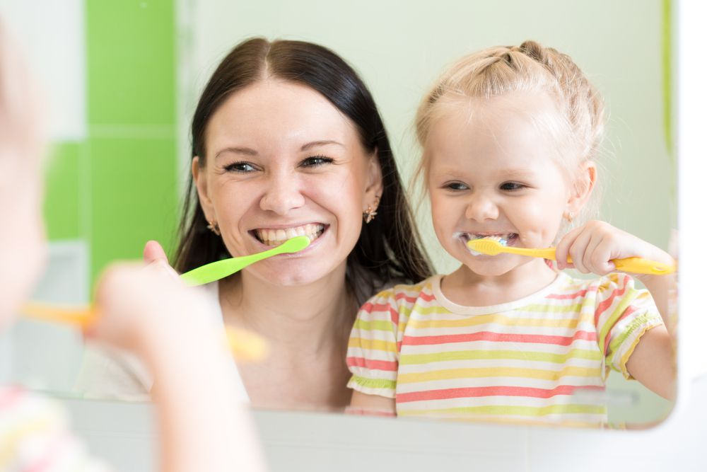 mom and baby looking into mirror and making it fun to brush teeth together