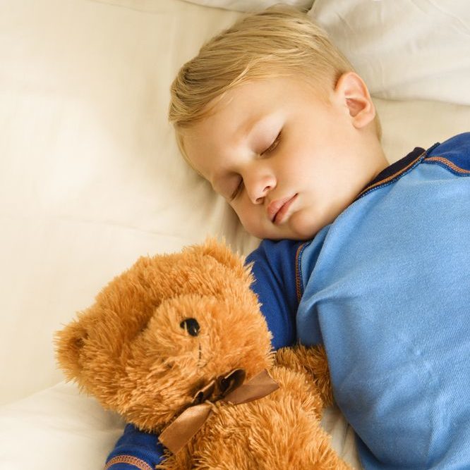 young toddler laying in bed and cuddling lovey teddy bear while he sleeps