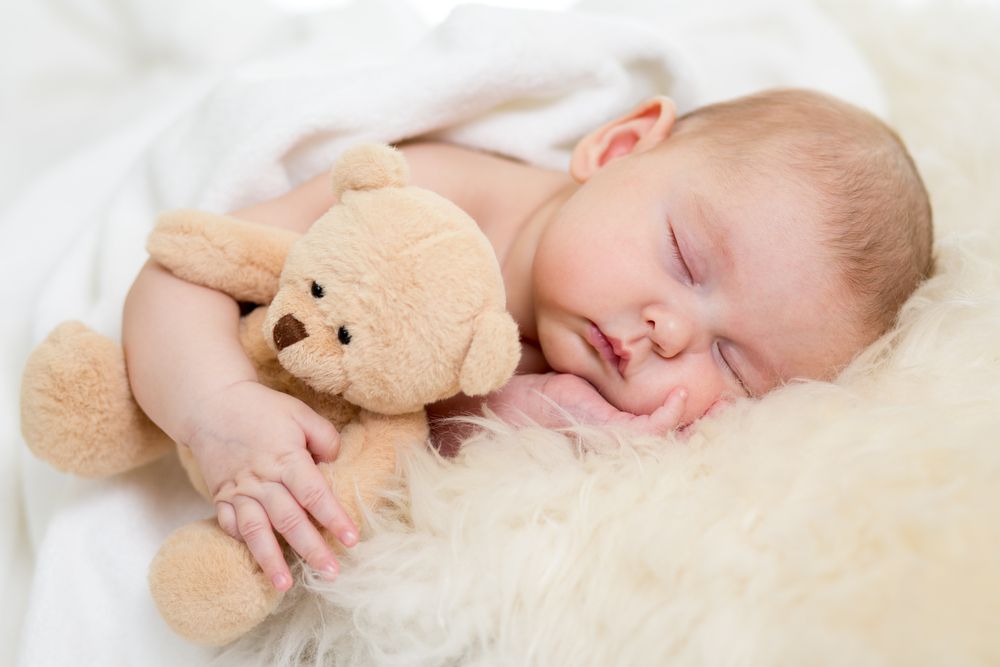 newborn sleeping on fur bed cuddling a lovey teddy bear