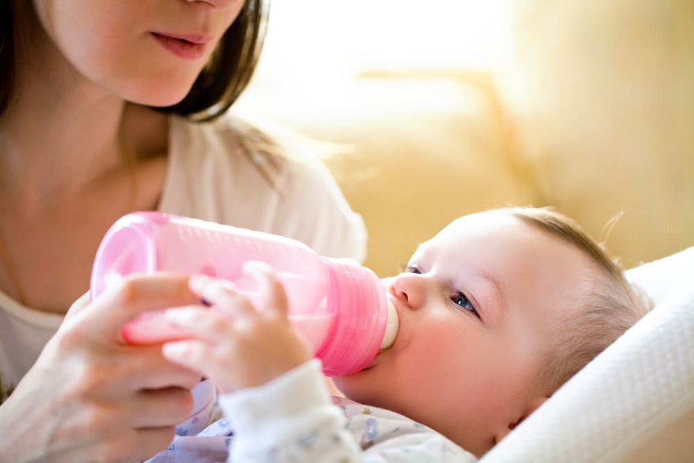 mom looking down at baby while feeding baby a bottle using paced bottle feeding