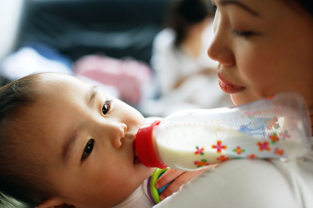asian mom looking down and while feeding baby using paced bottle feeding