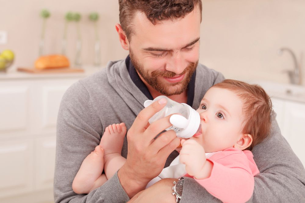 dad holding baby and smile while paced bottle feeding a bottle of milk