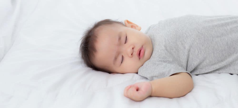 Baby sleeping independently in bed with arm up by his head